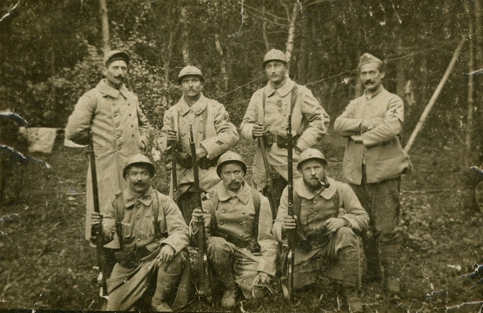 Achille Henri Mathias (au 1e rang, au milieu) au sein d'un groupe de soldats, casques sur la tête et fusil à la main, 1914-1917.